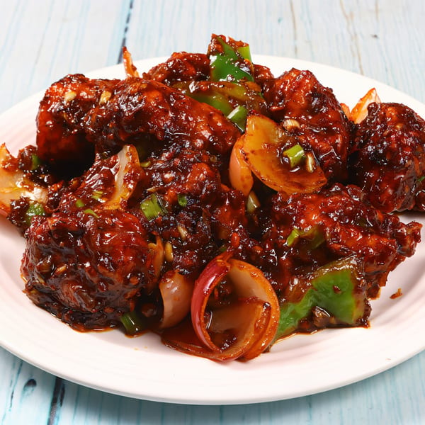 Close-up of Nepalese chili chicken with dark sauce, green peppers, and onions on a white plate.