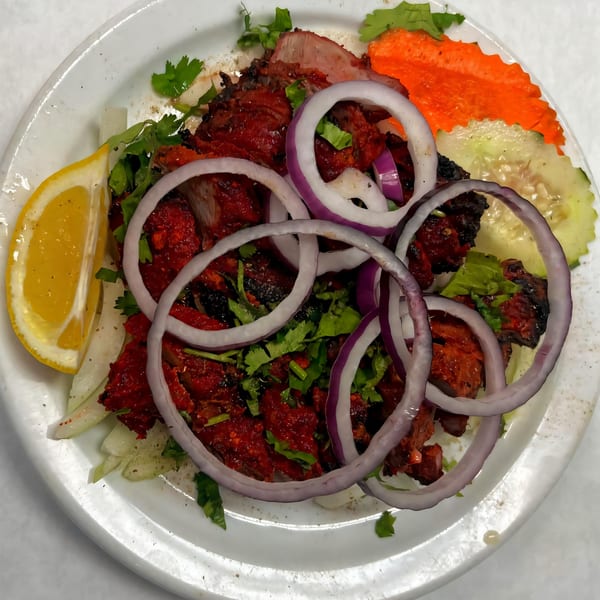 Taste of Nepal's spicy red chicken choila, garnished with red onion rings, cilantro, and a lemon wedge.
