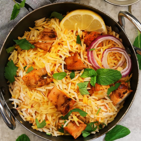 Nepalese chicken biryani with rice, lemon, red onion, and fresh herbs in a metal pot.