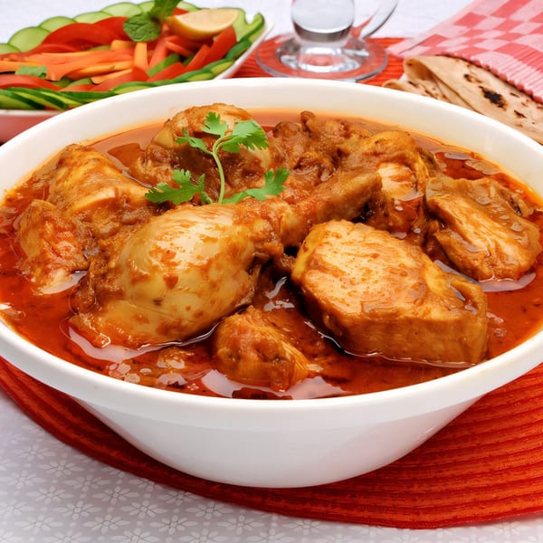 Nepalese chicken curry in a white bowl, with salad and flatbread in the background.