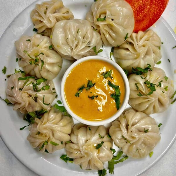A plate of Nepalese momos, garnished with cilantro, surrounding a bowl of orange dipping sauce.