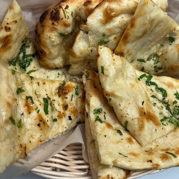 Basket of golden-brown naan bread, garnished with fresh green herbs, from Taste of Nepal.