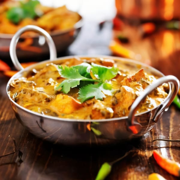 Nepalese chicken curry in a metal serving bowl, garnished with fresh cilantro on a wooden table.